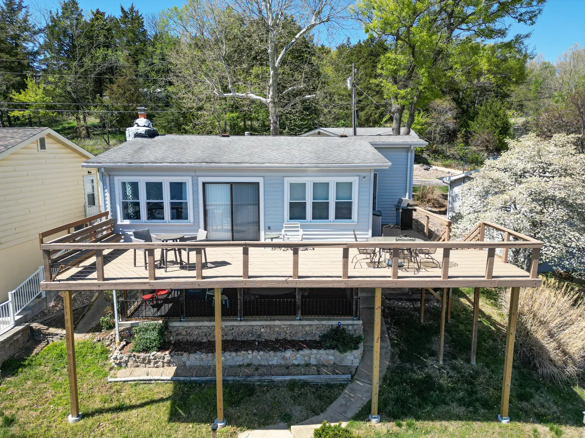This image showcases a spacious deck area with comfortable seating, part of the house's facade, and lush greenery surrounding the space. The setup is perfect for outdoor dining or relaxing, with an ambiance that invites residents to enjoy the lake views while seamlessly connecting interior comforts to the outdoors.