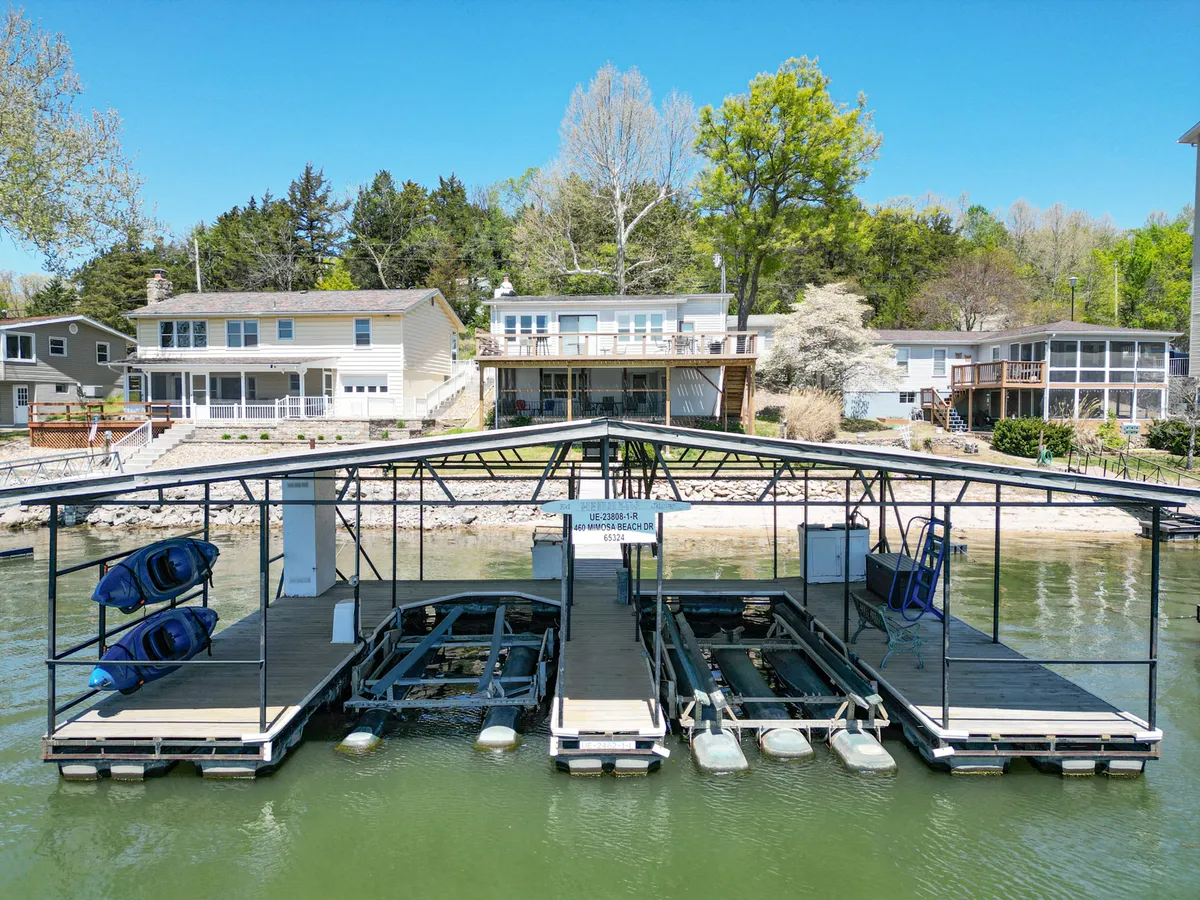 An exterior image featuring a spacious boat dock equipped with kayaks and framed by surrounding homes and trees. The scene suggests readiness for kayaking, fishing, and family-friendly waterfront activities.