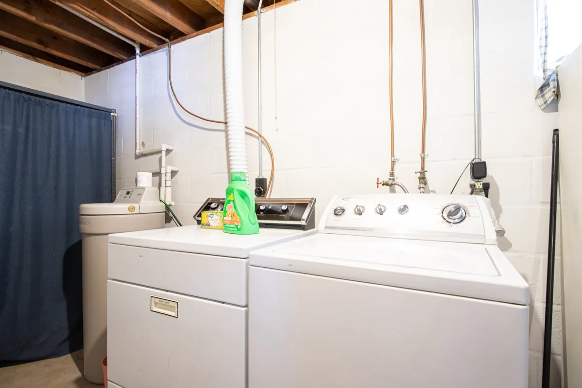 This image displays a practical laundry space featuring a washing machine, dryer, utility sink, and a detergent bottle. The area is organized and functional, representing the in-home laundry amenities available to guests.