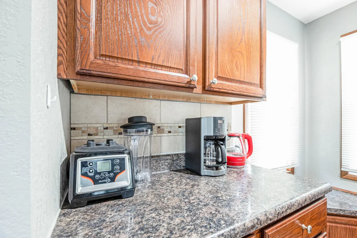 A close-up of a kitchen area featuring a coffee maker, kettle, blender, granite countertop, and warm wooden cabinetry. The setup exudes hospitality and convenience, perfect for morning routines and gathering with loved ones.