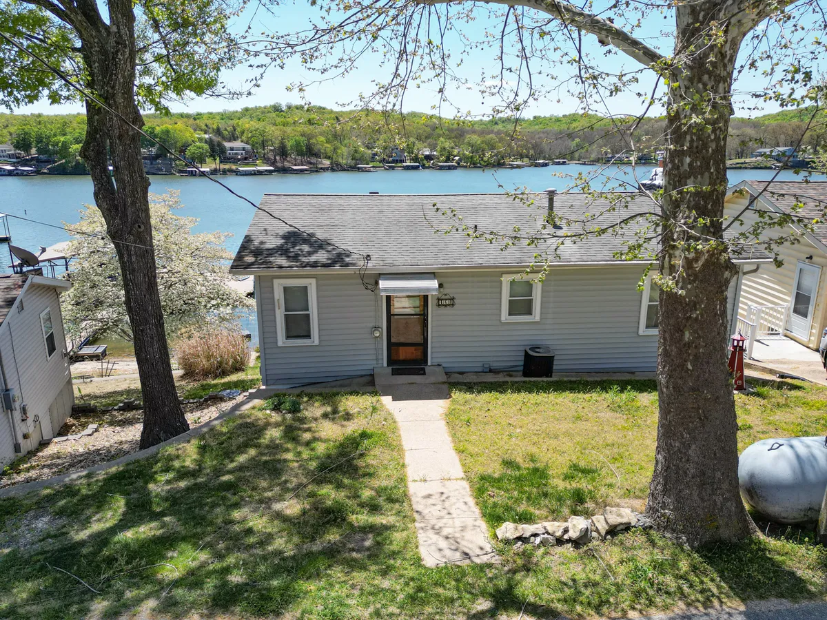 A peaceful exterior shot of the front entrance of the house, with the gentle water view visible beyond and vibrant greenery on either side. The image hints at the friendly, welcoming atmosphere of the neighborhood and the seamless blend of private relaxation and community connection.