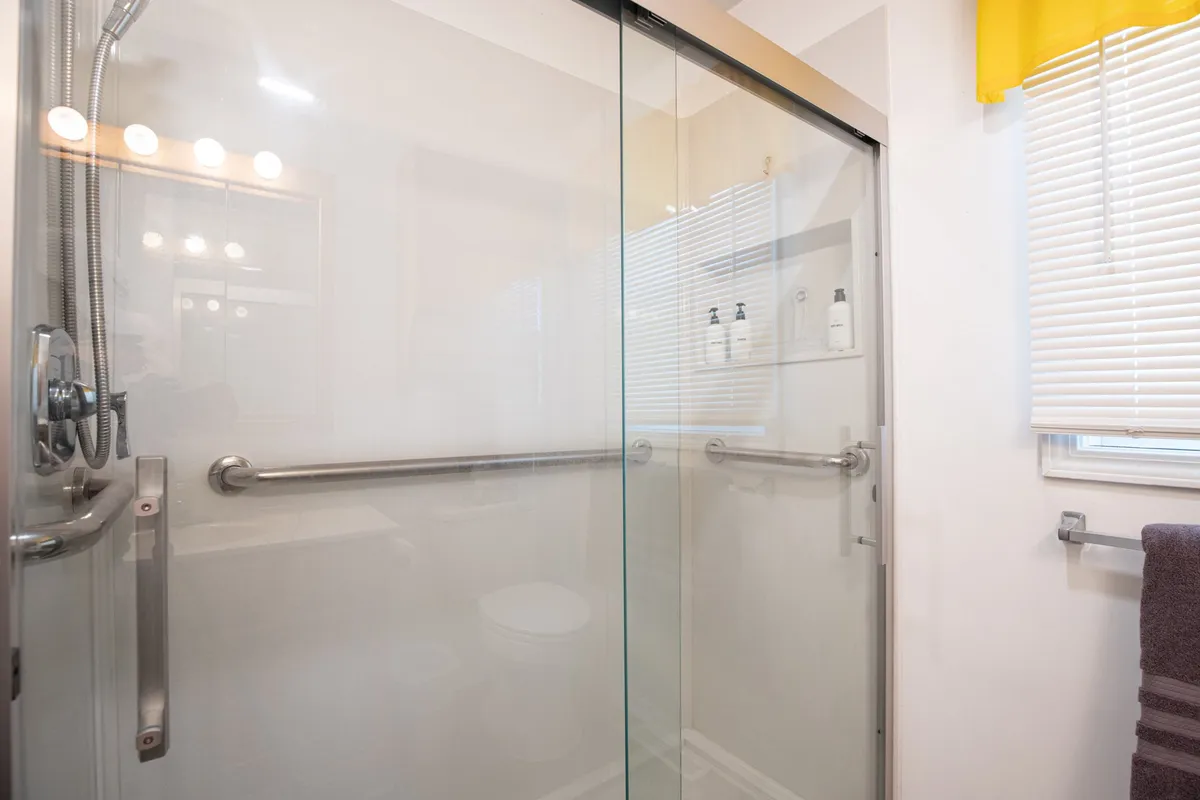 A serene bathroom featuring a glass shower enclosure, bright yellow curtain for a pop of color, and vanity lighting. The space feels fresh, well-appointed, and inviting for a calming self-care routine.