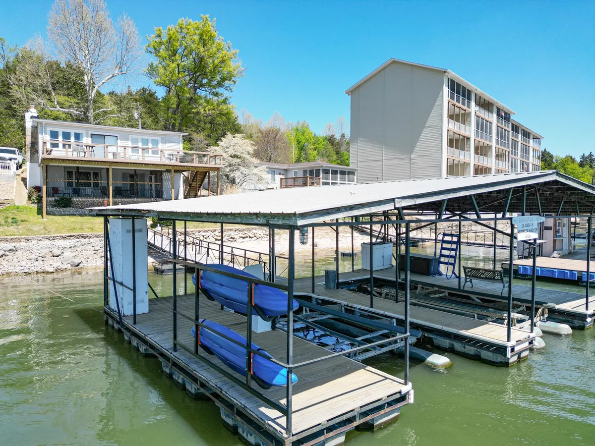 This exterior image displays a dock with boats moored beside a two-story house, surrounded by lush trees. The setting is tranquil, with the water gently reflecting the evening sky, evoking the feeling of lakeside leisure and access to boating activities.