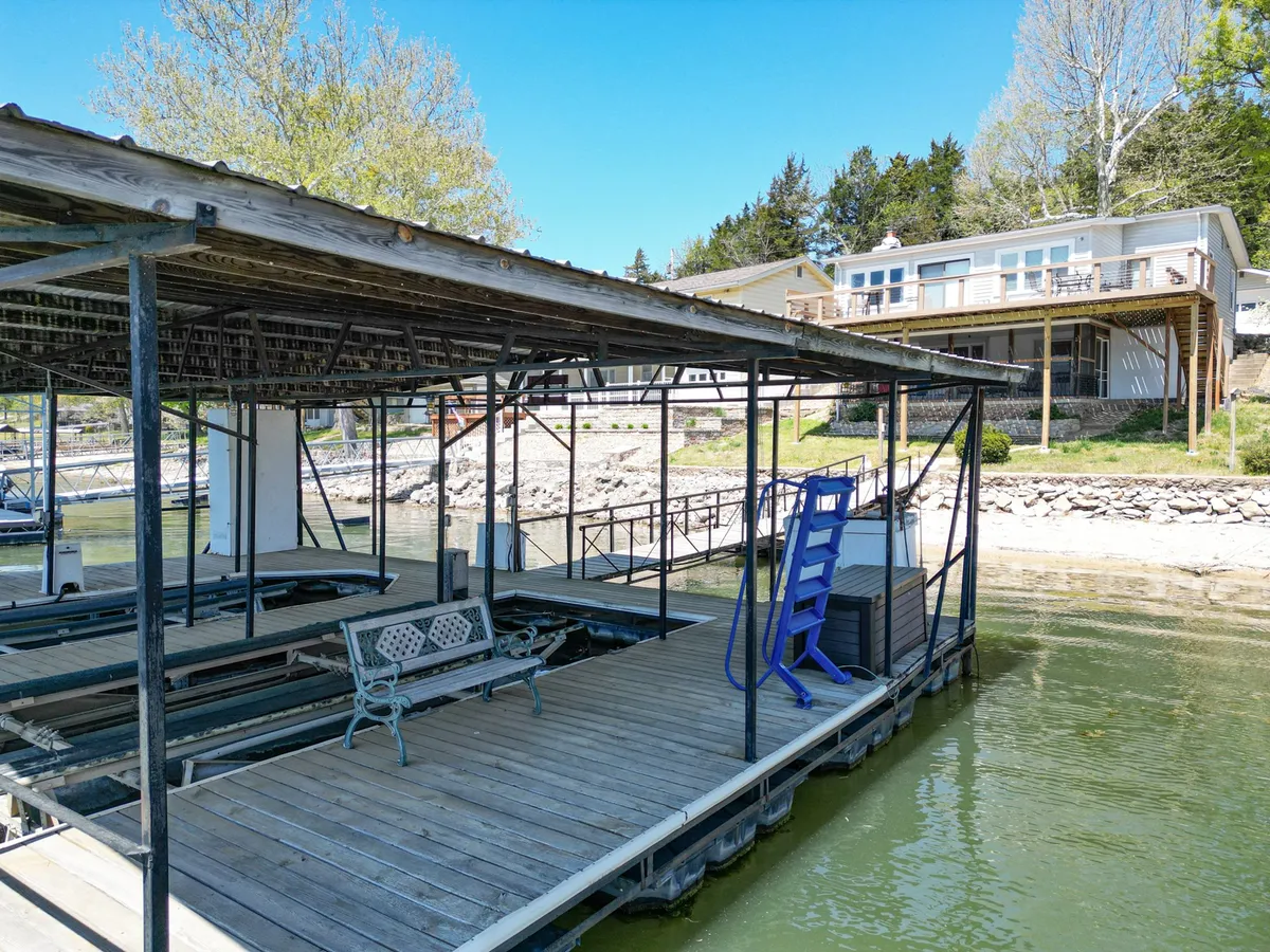 The focus here is on a private dock jutting out into the lake, with boats tied nearby, a blue slide for water fun, and a bench offering a peaceful vantage point. The tranquil water and open sky embody the waterfront lifestyle, and the dock is perfect for both relaxation and launching aquatic adventures.