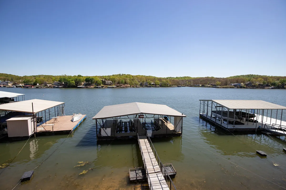 A view of a private dock extending into the calm lake, with boathouses visible in the background and serene water inviting for swimming, boating, and relaxing. The dock is the central feature, emphasizing easy access to water activities directly from the property.