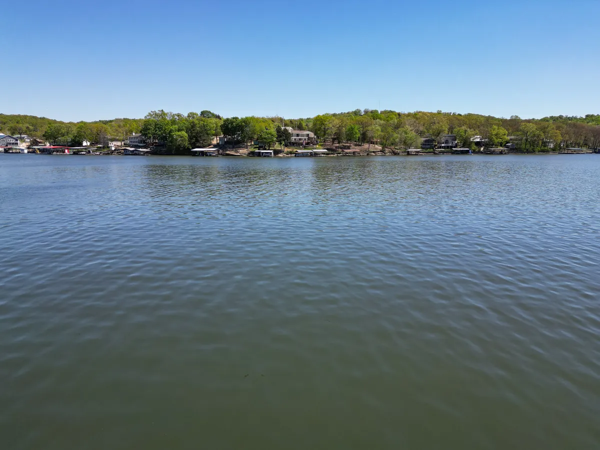 A wide view of the calm lake surface bordered by lush green trees and waterfront homes. The peaceful scenery hints at boating, fishing, and lakeside exploration, inviting viewers to imagine their own lakeside adventures.