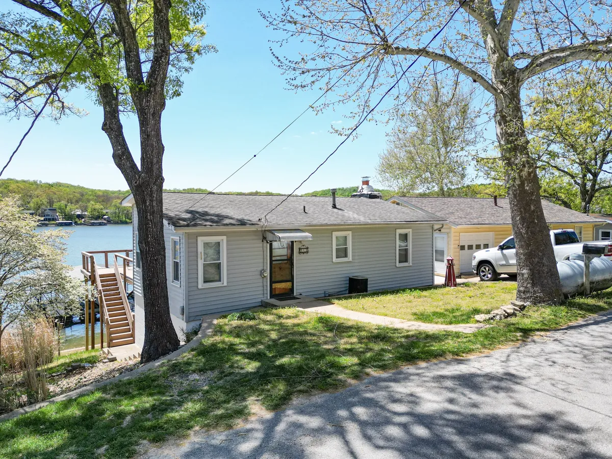 A wide exterior view showcasing the house, with the sparkling lake in the background, surrounded by trees and a pathway leading toward the water. The image captures the home’s immediate connection to the lake and its integration within lush, natural surroundings.